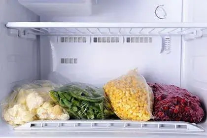 Interno di un frigorifero AEG con verdure e mais confezionati su ripiano, luce bianca e sportello aperto.