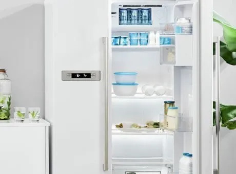 Frigorifero bianco aperto con ripiani, contenitori e vaschette, luce interna e bottiglie sulla porta.