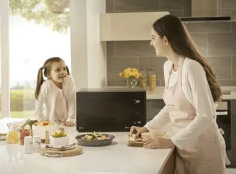 Due persone in cucina moderna preparano il cibo con un microonde LG, una bambina e una donna con grembiule bianco.